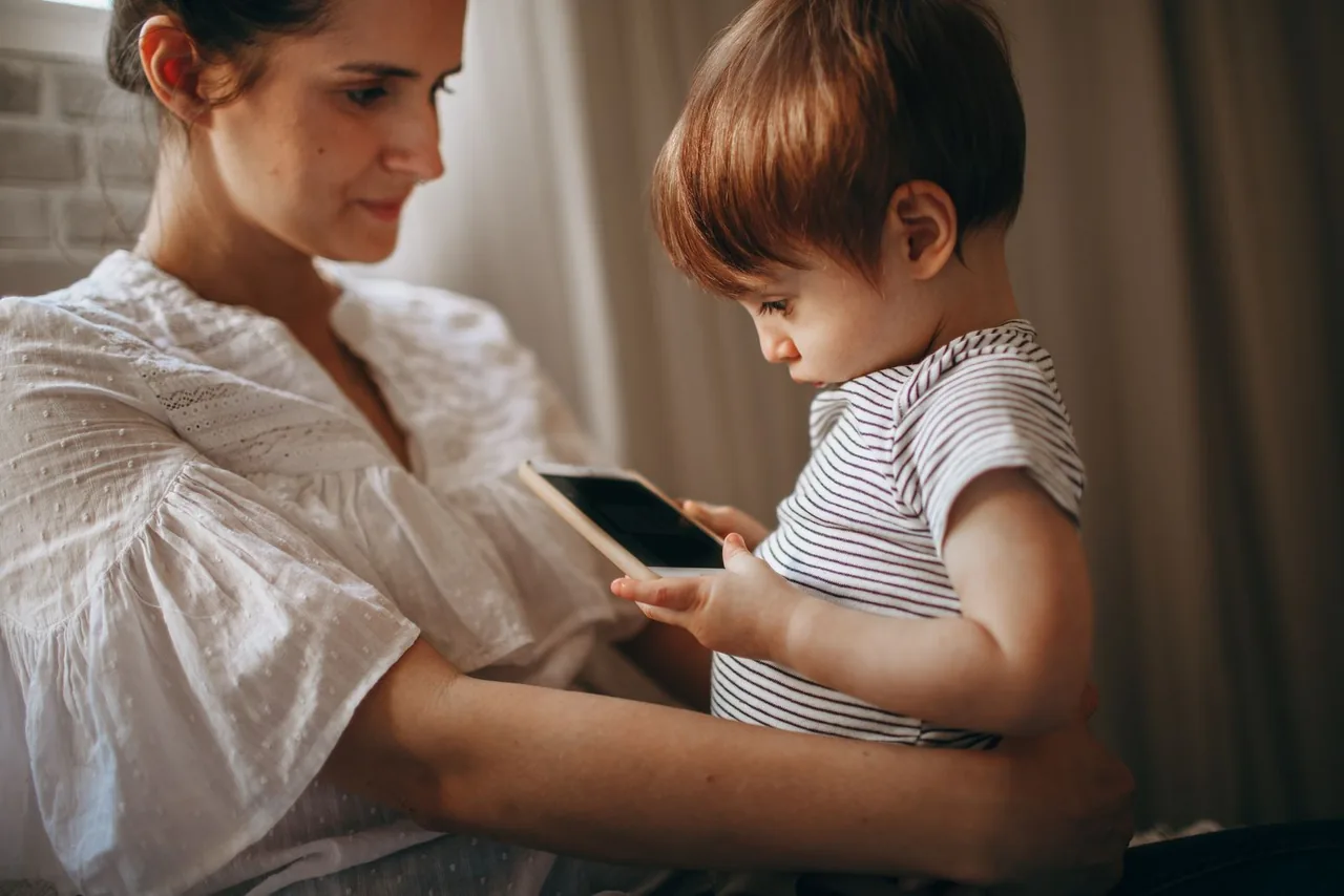 A mother and young child looking at a smartphone together at home.
